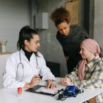 Médico conversa com uma paciente em recuperação do câncer e uma pessoa próxima em casa.