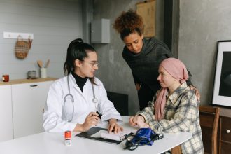Médico conversa com uma paciente em recuperação do câncer e uma pessoa próxima em casa.