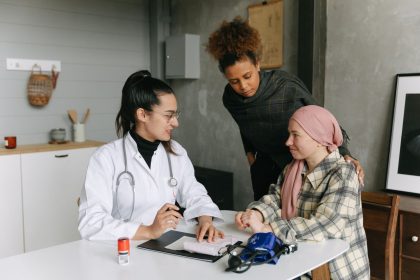 Médico conversa com uma paciente em recuperação do câncer e uma pessoa próxima em casa.