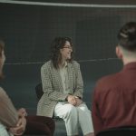 Grupo diverso de adultos participa de uma discussão em roda em um ambiente interno.