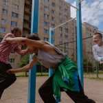 Grupo diverso de adolescentes brinca em um playground ao ar livre sob um céu azul.