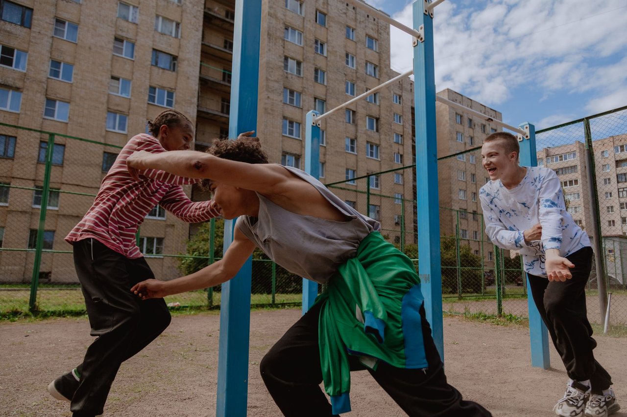 Grupo diverso de adolescentes brinca em um playground ao ar livre sob um céu azul.