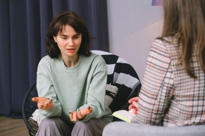 Mulher participa de uma entrevista em uma sala iluminada, diante de outra mulher que a escuta atentamente.