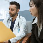 Médico conversa com uma paciente enquanto analisa registros de saúde em um consultório.