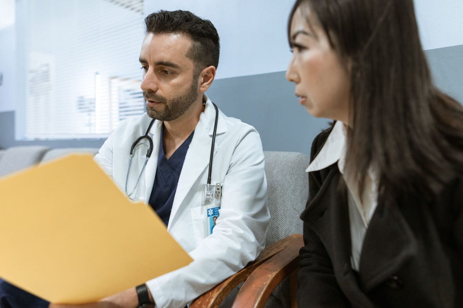 Médico conversa com uma paciente enquanto analisa registros de saúde em um consultório.