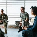 Grupo de militares veteranos participa de uma sessão coletiva de apoio psicológico com um profissional de saúde mental.