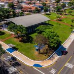 Vista aérea de um parque arborizado integrado à malha urbana, com ruas e edificações ao redor.