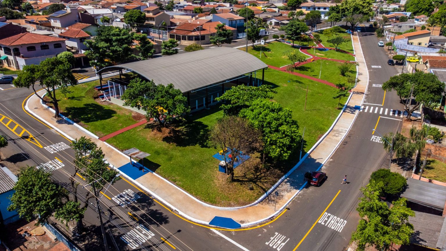 Vista aérea de um parque arborizado integrado à malha urbana, com ruas e edificações ao redor.